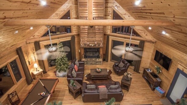 A spacious loft-style living area with a high ceiling, wooden beams, a fireplace, a pool table, and a Christmas tree.