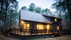 A log cabin with a metal roof, wooden deck, and a staircase leading to the entrance.