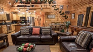 A cozy cabin interior with a wooden interior, a dining area, a kitchen, and a living room with leather sofas and a coffee table.