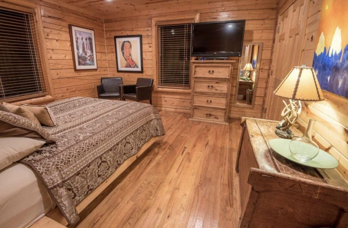 A wooden cabin-style bedroom with a bed, dresser, TV, and artwork on the walls.