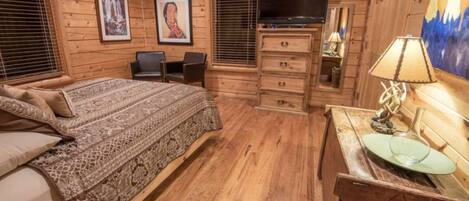 A wooden cabin-style bedroom with a bed, dresser, TV, and artwork on the walls.
