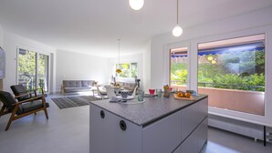 A modern kitchen with a central island, large windows with a view of greenery, and a dining area with a sofa and table. - Coloratura Frontlake Lugano with Terrace, Paradiso (Lugano), Switzerland (Paradiso (Lugano))