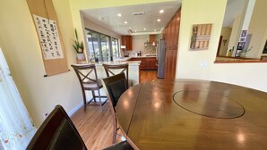 Un comedor con mesa y sillas de madera, una cocina al fondo y un tablón de anuncios con texto.