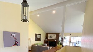 Amplia sala de estar con piso de madera, un sofá, una mesa de centro y una chimenea. Una escalera conduce a un nivel superior.