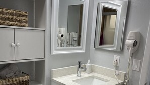 Een moderne badkamer met een wit wastafelmeubel, wc en wastafel. Op de plank staan rieten manden, een haardroger zit aan de muur en er is een prullenbak.