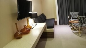 A modern hotel room with a flat-screen TV, a sofa, a dining table with chairs, and decorative vases on a console table. - Nice Studio, Located a few Steps From the 5th av (Playa del Carmen)