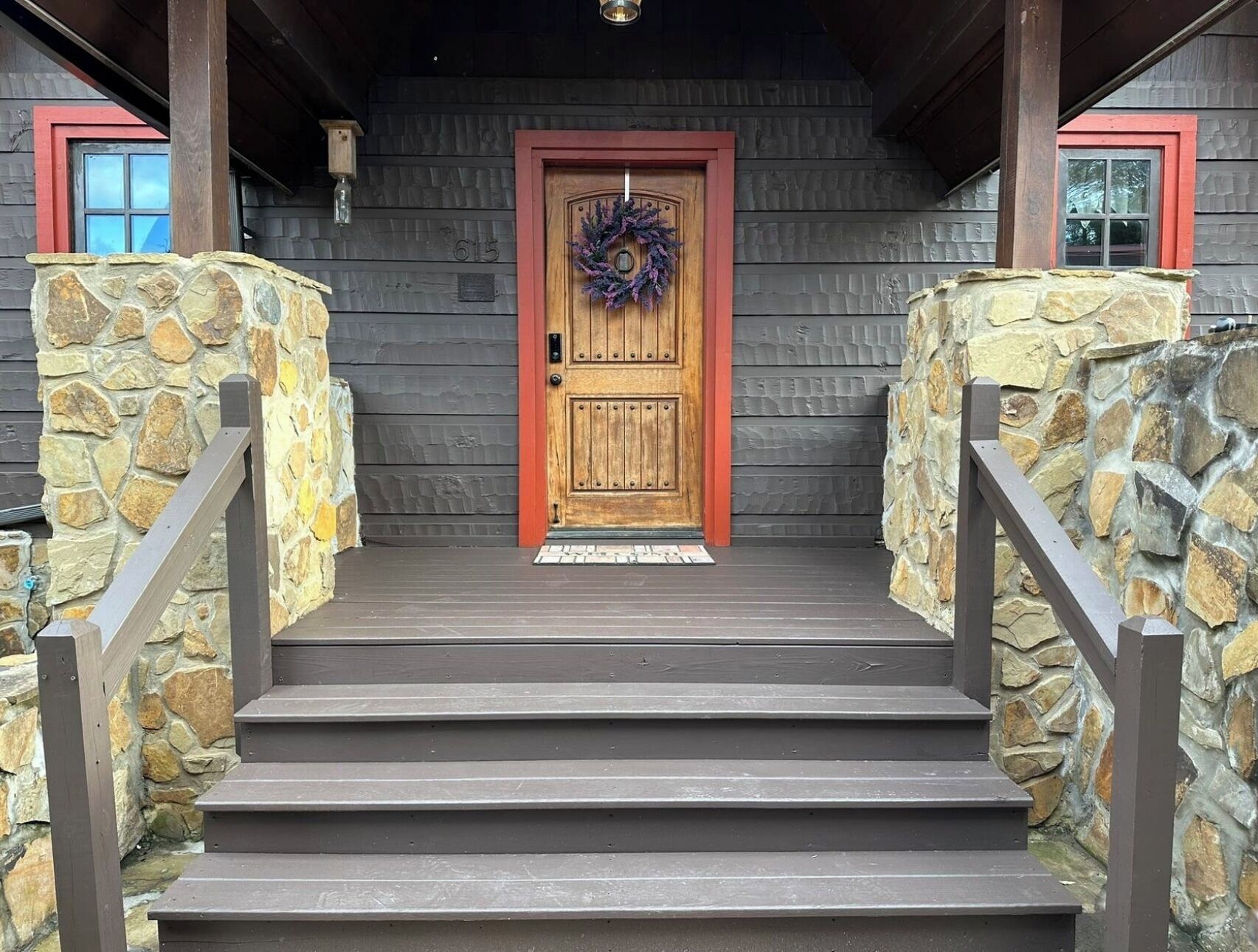 A wooden front door with a wreath, flanked by stone walls and wooden steps leading up to it.