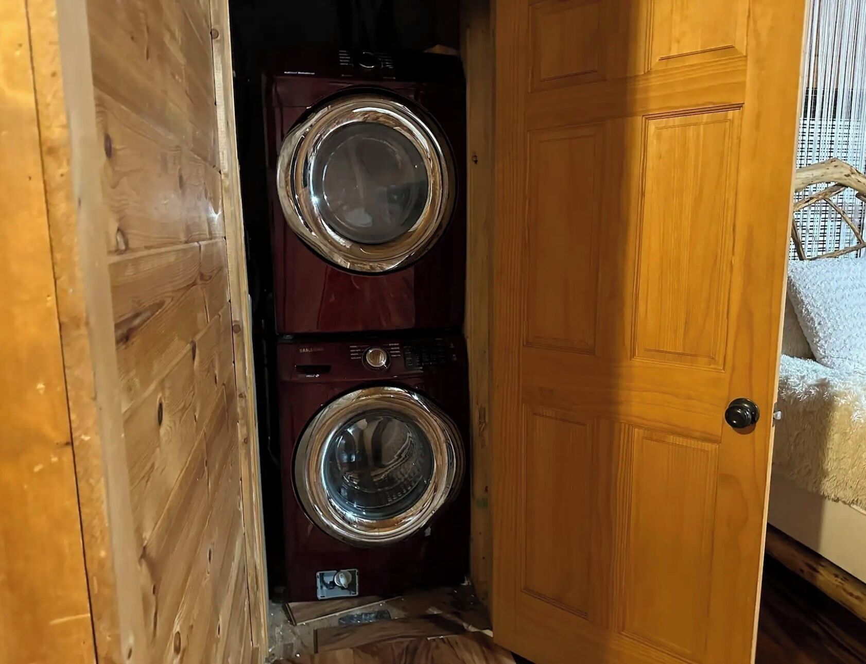Uma porta de madeira dá acesso a uma lavanderia com duas máquinas de lavar roupa empilhadas.