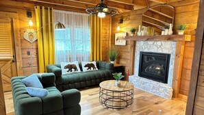 Interior acogedor de una cabaña con un sofá verde, chimenea, piso de madera y ventilador de techo.