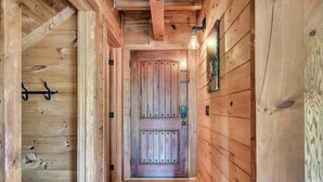 Un pasillo de madera con una puerta central, paredes de madera y una lámpara arriba.