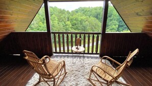 Una terraza de madera con dos mecedoras y una mesita, con vistas a un área boscosa.