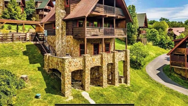 Una cabaña de troncos de varios pisos, con base de piedra, balcones y una terraza de madera alrededor.