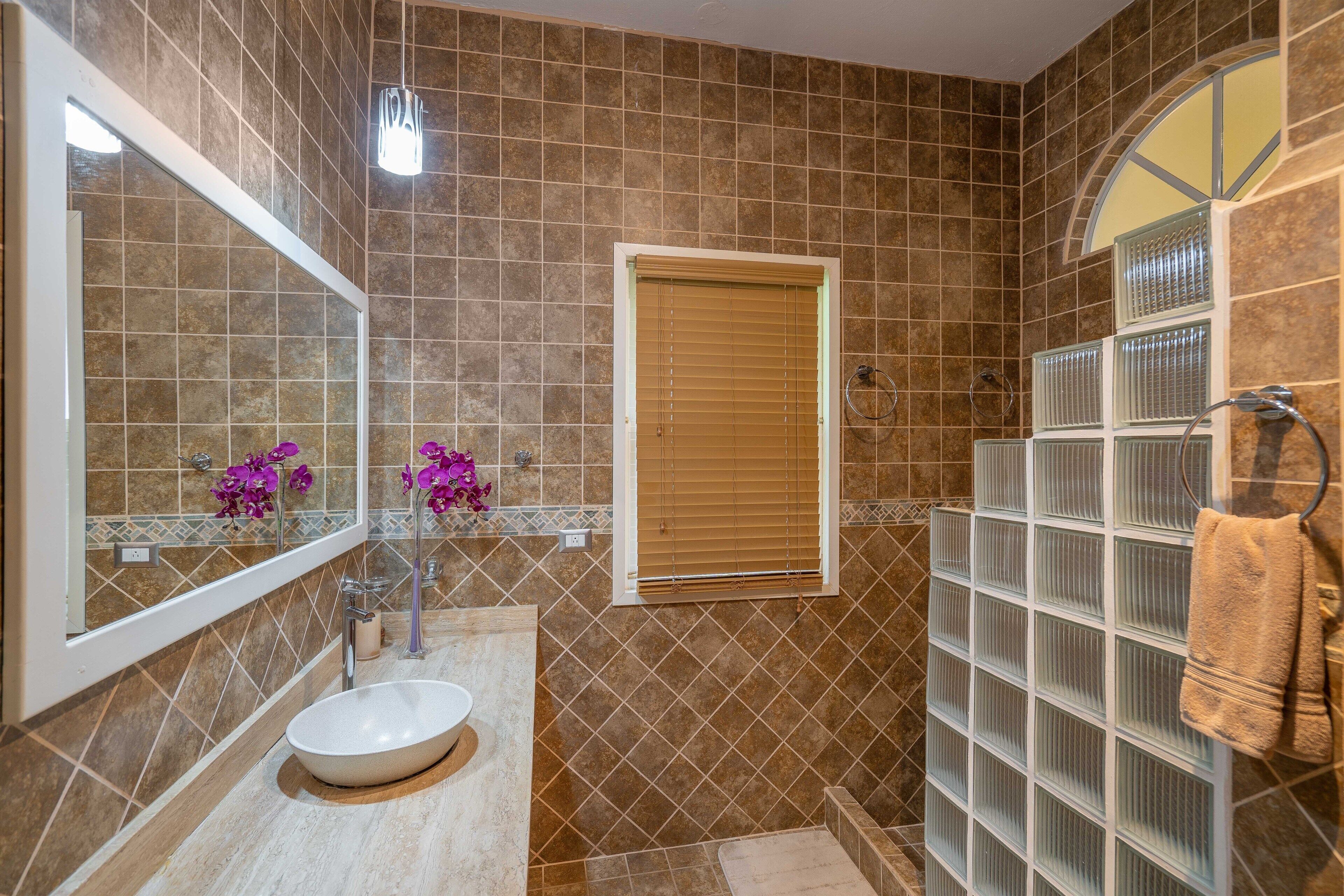 A bathroom with a large mirror, a sink, a window, and a shower area.