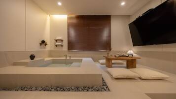 A modern bathroom with a large bathtub, a wooden vanity, and a flat-screen TV mounted on the wall.