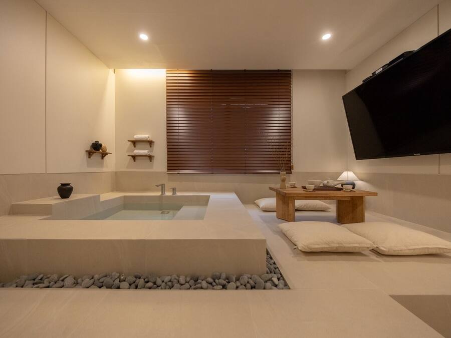 A modern bathroom with a large bathtub, a wooden vanity, and a flat-screen TV mounted on the wall.
