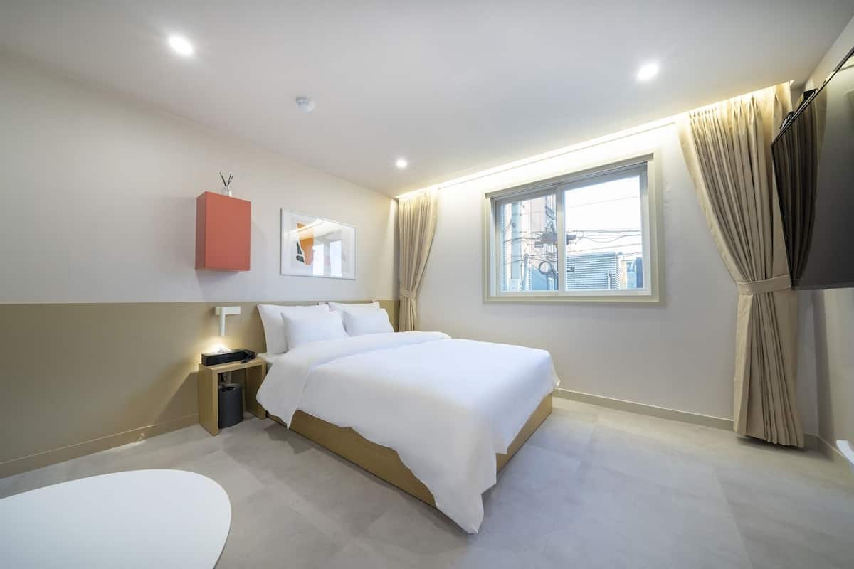 Habitación de hotel moderna con una cama grande, una mesita de noche, una pequeña mesa y una ventana con cortinas.