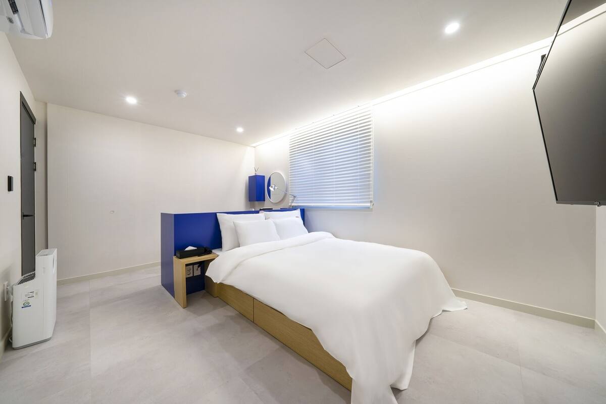 Un dormitorio moderno con cama, mesita de noche y televisor montado en la pared.