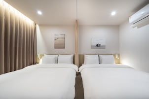 A hotel room with two beds, beige curtains, a ceiling light, and two wall-mounted paintings.