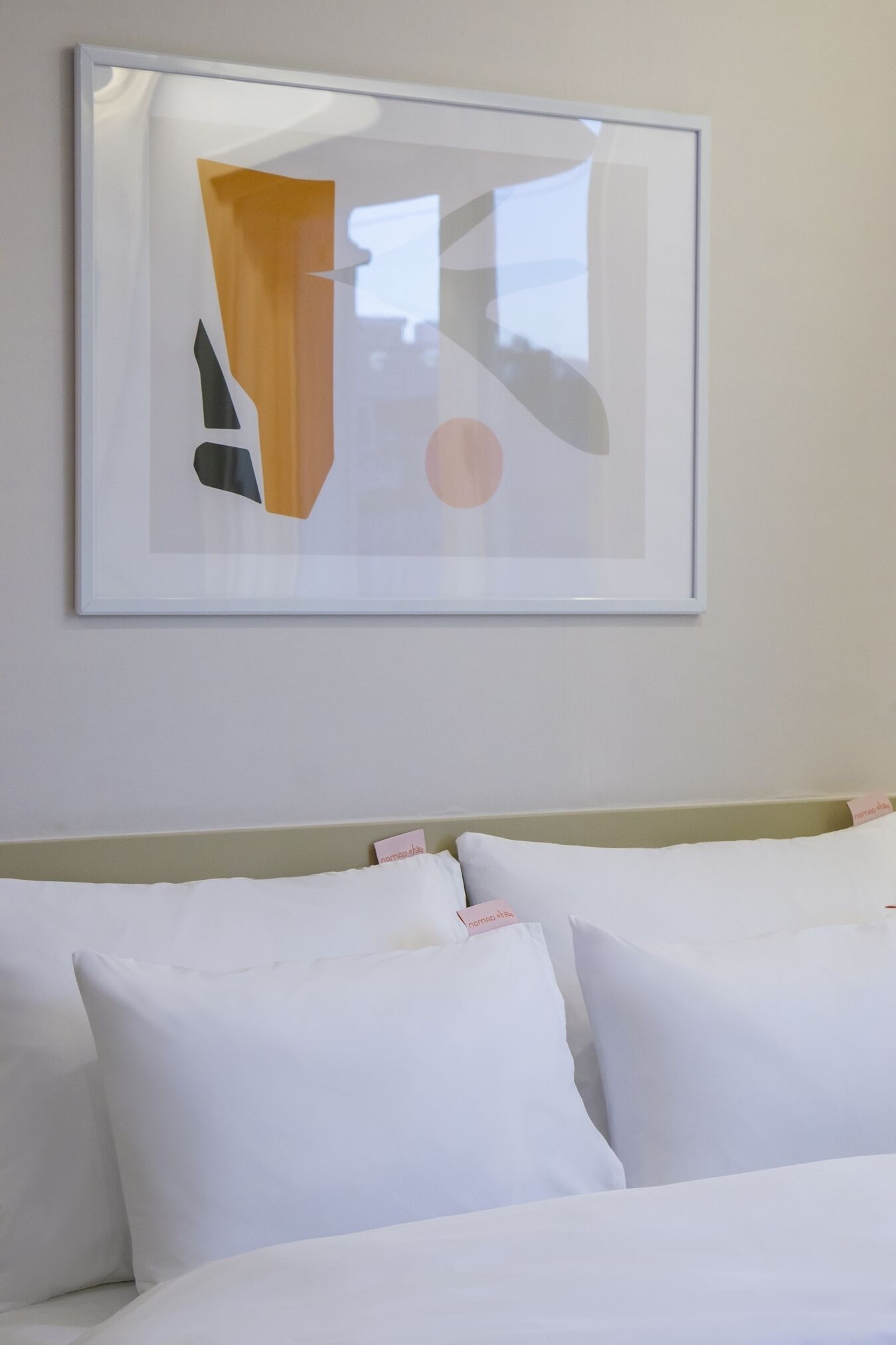 A hotel room with a bed, pillows, and a framed abstract artwork on the wall.