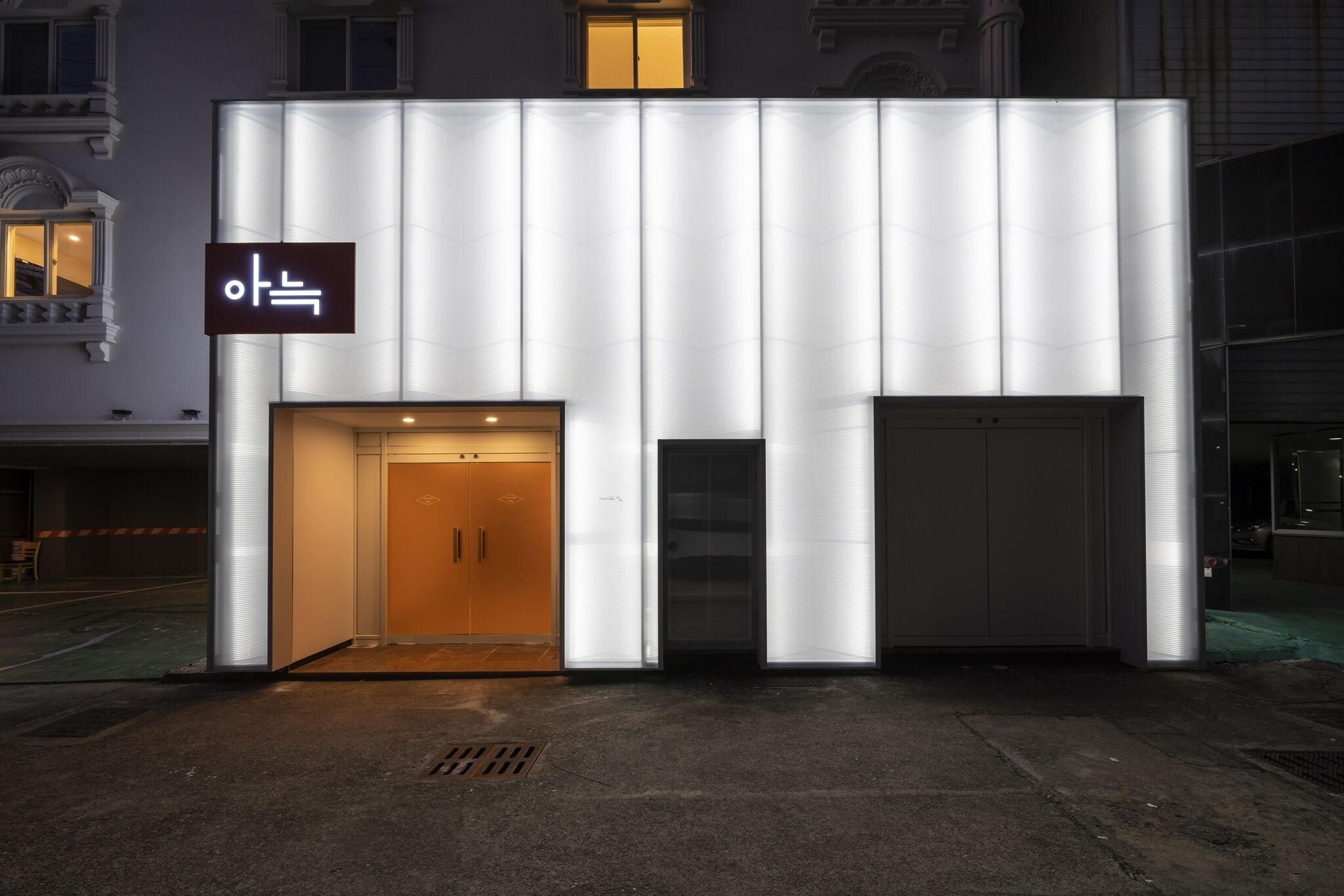 Um edifício moderno com uma grande placa iluminada, entrada de vidro e porta de garagem.