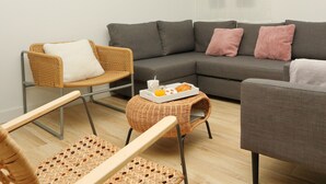 A modern living room with a grey sofa, a wicker chair, and a small round table with breakfast items.