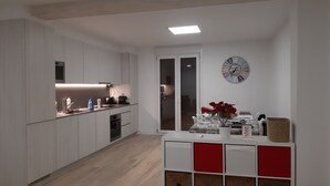 A modern kitchen with white cabinets, a wooden floor, and a dining area with a white table and red accents.