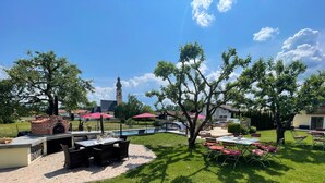 Un espace patio agrémenté d’un barbecue en briques, de sièges d’extérieur et offrant une vue sur le clocher d’une église.