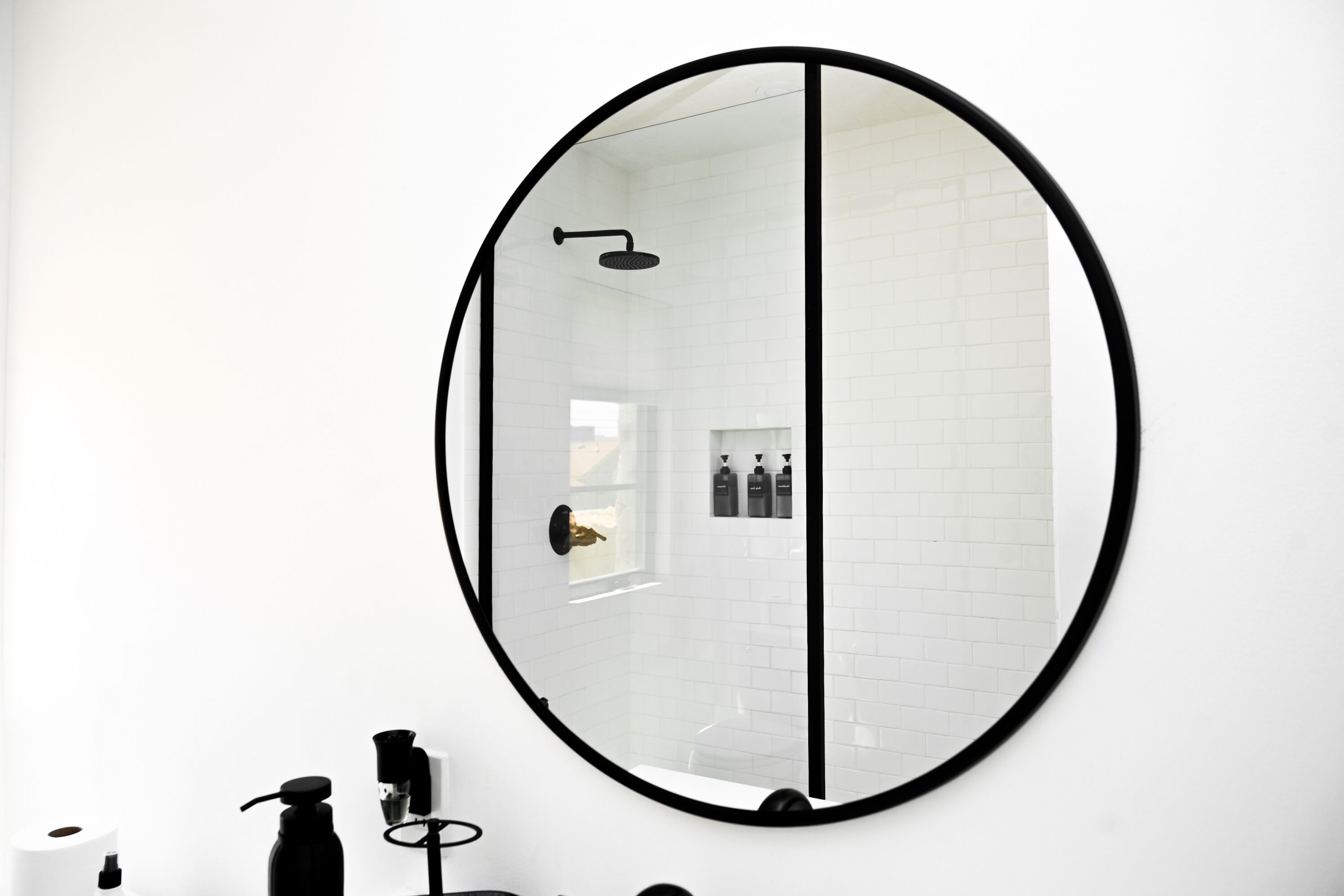 A bathroom with a large oval mirror, white tiled walls, a shower, and a toilet.