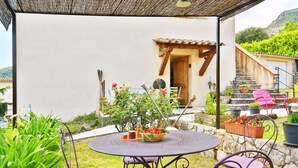 Eine Terrasse mit rundem Tisch und violetten Stühlen, umgeben von Kübelpflanzen und einer Holzpergola.