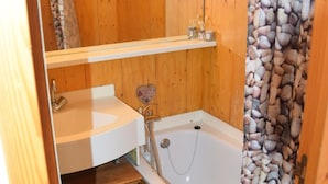 Un baño pequeño con un tocador de madera, una bañera y una cortina de ducha con diseño de piedras.