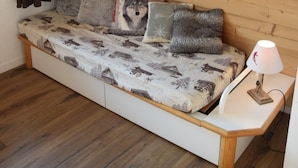 Una habitación acogedora con pared de madera, cama con ropa de cama estampada, un cuadro colgado y una lámpara de noche.