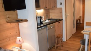 Un espacio habitable compacto con kitchenette, un televisor montado en una pared de madera, un pequeño comedor y una cama con cubrecama estampado.
