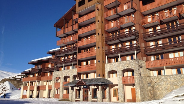 Un hotel de varios pisos con balcones, fachada de piedra y vistas a una pista de esquí.