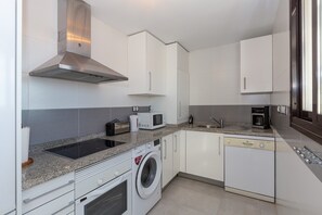 Une cuisine moderne avec des armoires blanches, une hotte de cuisinière en acier inoxydable, un lave-linge intégré, un four à micro-ondes et un lave-vaisselle.