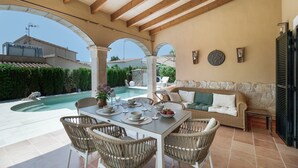 Une terrasse extérieure avec une piscine, une table à manger, des chaises en osier et un canapé.