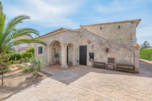 A stone building with a tiled roof, a paved entrance, and a bench outside.