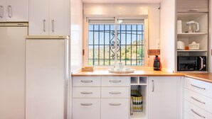A kitchen with white cabinets, a window with a metal grill, a coffee maker, and a microwave. - Holiday Home 'New House In Malaga Nature' with Mountain Views, Wi-Fi and Air Conditioning (Málaga)