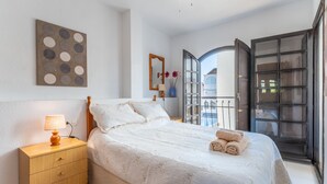 A bedroom with a bed, bedside table, lamp, and a view through an open door. - Apartment El Paraiso near Beach with Shared Pool, Balcony, & Wi-Fi (Torrevieja)