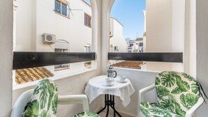 A balcony with two chairs, a table, and a view of a white building with a tiled roof. - Apartment El Paraiso near Beach with Shared Pool, Balcony, & Wi-Fi (Torrevieja)