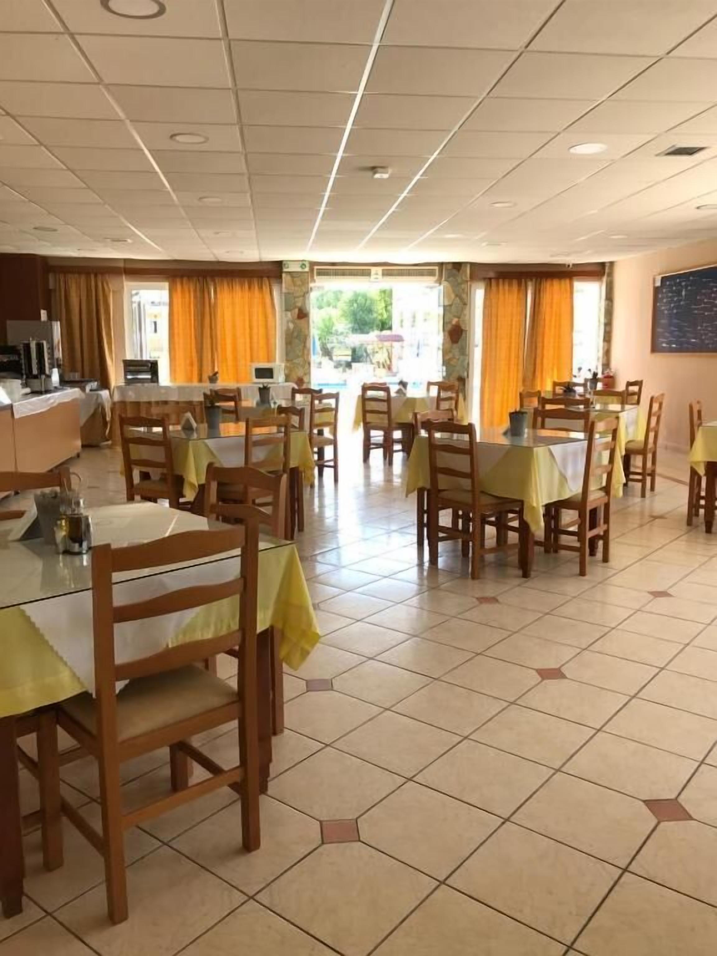 Un comedor con varias mesas y sillas, un área de cocina y vistas al exterior.