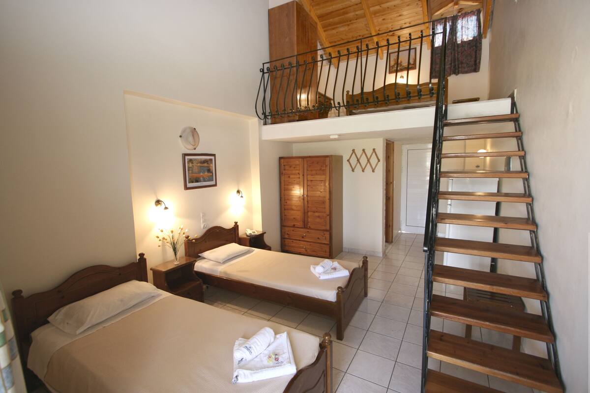 A hotel room with two beds, a wooden staircase, and a balcony with a railing.