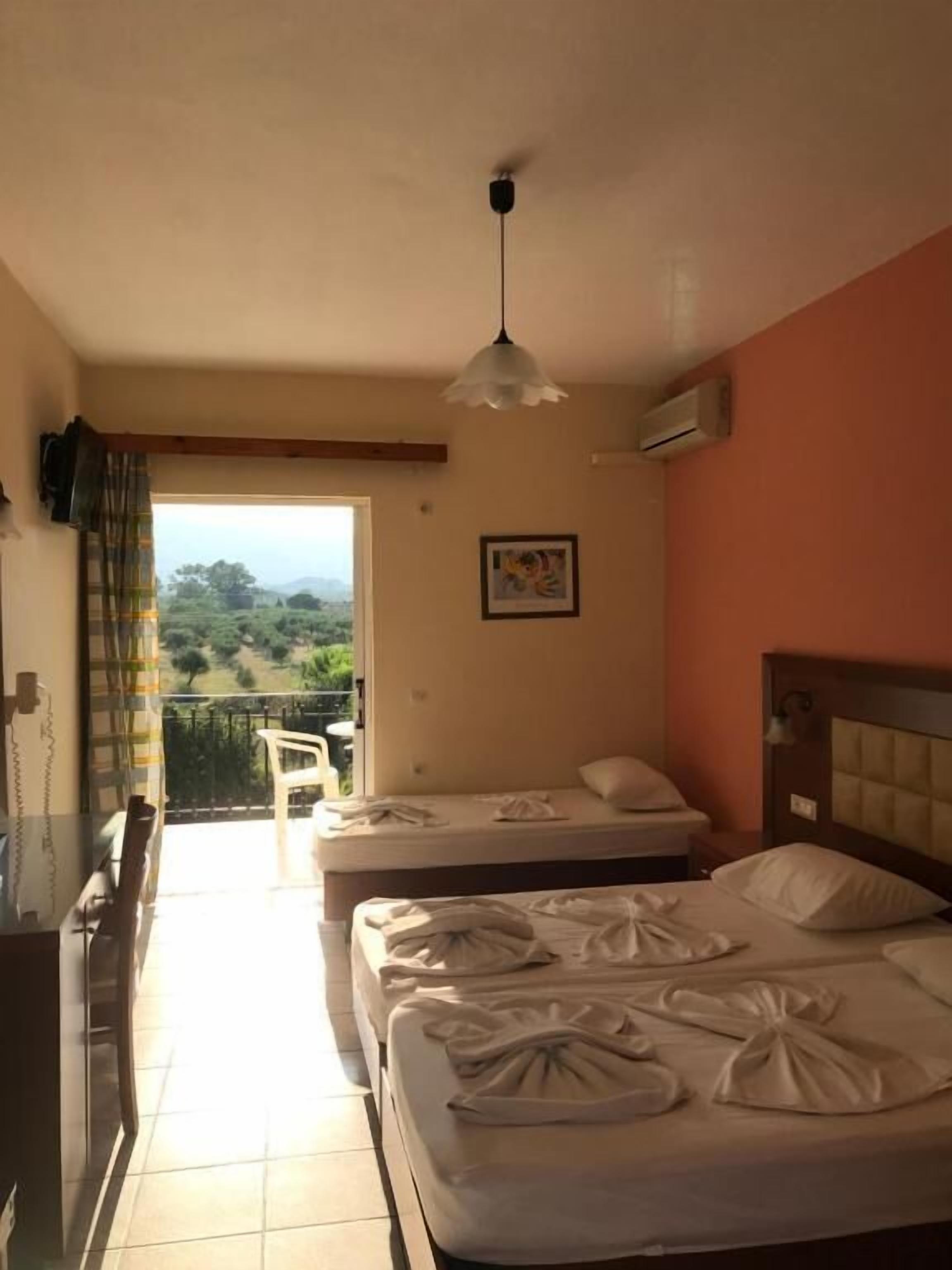 Une chambre d’hôtel avec deux lits, un balcon, un ventilateur de plafond et un tableau au mur.