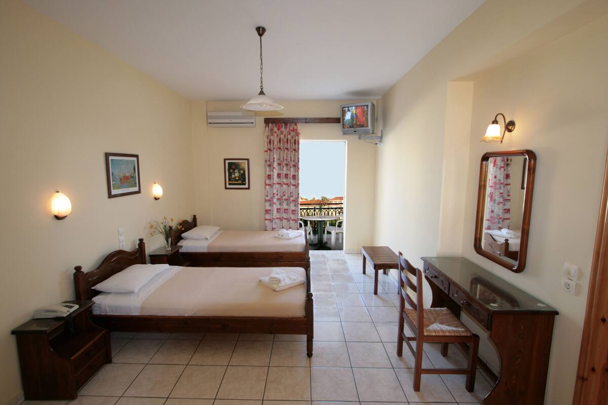 A hotel room with two beds, a desk, a chair, a TV, and a balcony with a view.