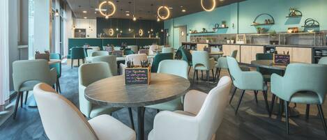 Interior moderno de una cafetería con mesas redondas, sillas e iluminación colgante.