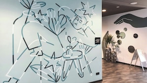 Una pared con arte abstracto, una escultura de mano y una pequeña mesa con una planta.