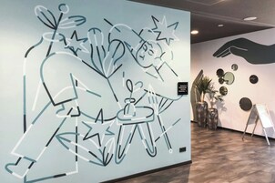 Paredes com arte abstrata, uma escultura de mão e uma pequena mesa com uma planta.