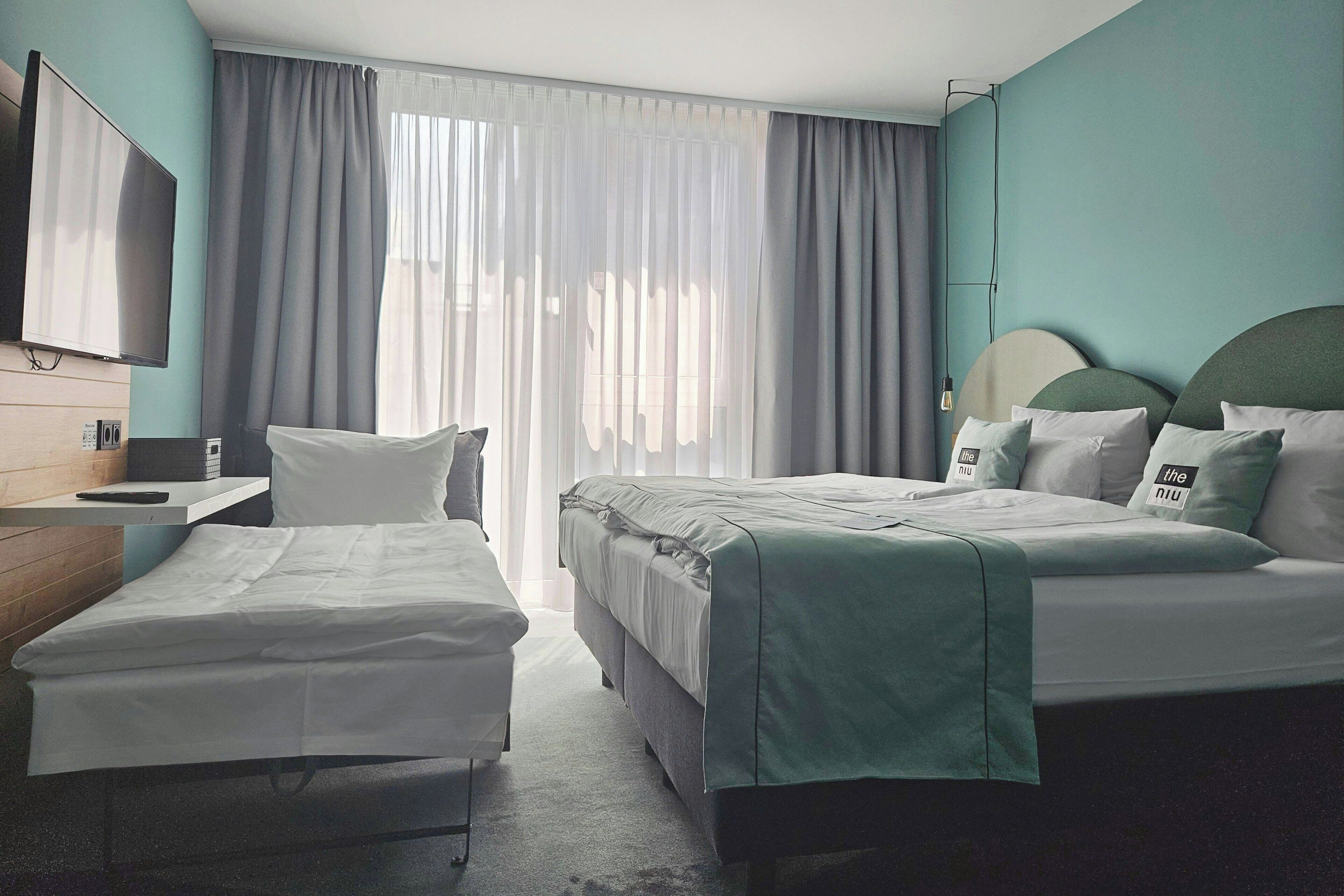 A hotel room with a bed, a bedside table, a TV, and a window with curtains.
