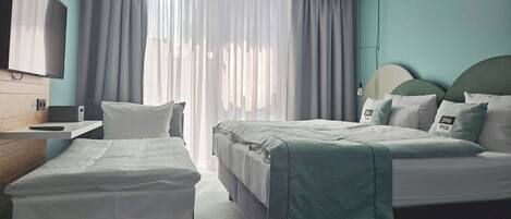 Una habitación de hotel con cama, mesita de noche, televisión y ventana con cortinas.