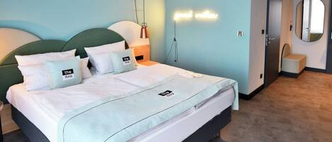 Una habitación de hotel moderna con cama, mesita de noche, lámpara, espejo y puerta.