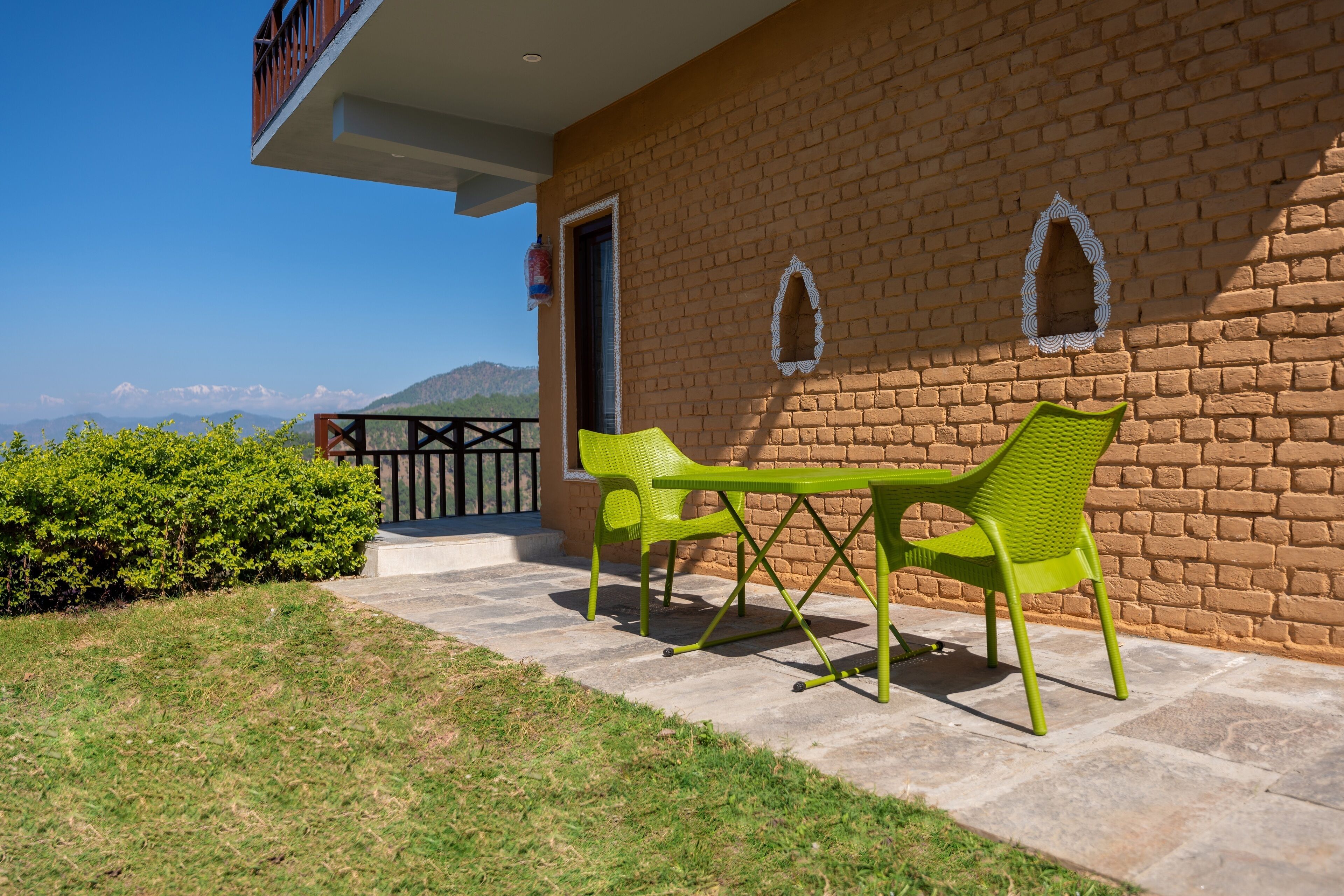 Un patio con dos sillas verdes y una mesa, un muro de ladrillo y vistas a las montañas.